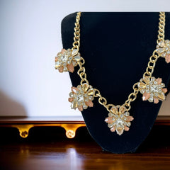 Gold tone statement necklace with five floral pendants featuring peach, champagne, and clear crystals in marquise, square, pear, and chaton cuts; adjustable curb chain with lobster clasp.