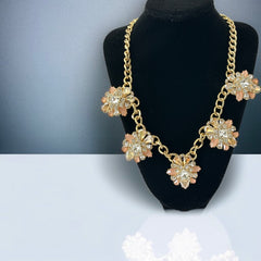 Gold tone statement necklace with five floral pendants featuring peach, champagne, and clear crystals in marquise, square, pear, and chaton cuts; adjustable curb chain with lobster clasp.