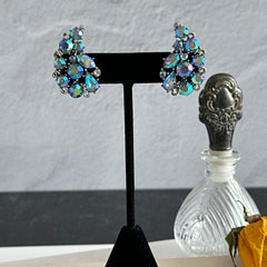 Vintage Lisner silver tone clip-on earrings with blue Aurora Borealis rhinestones in a leaf-shaped climber design, shown in various arrangements.