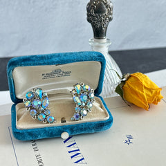 Vintage Lisner silver tone clip-on earrings with blue Aurora Borealis rhinestones in a leaf-shaped climber design, shown in various arrangements.