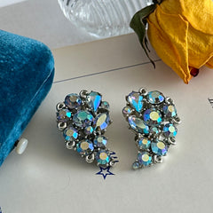 Vintage Lisner silver tone clip-on earrings with blue Aurora Borealis rhinestones in a leaf-shaped climber design, shown in various arrangements.
