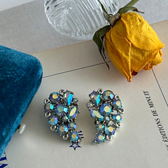 Vintage Lisner silver tone clip-on earrings with blue Aurora Borealis rhinestones in a leaf-shaped climber design, shown in various arrangements.