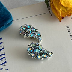 Vintage Lisner silver tone clip-on earrings with blue Aurora Borealis rhinestones in a leaf-shaped climber design, shown in various arrangements.