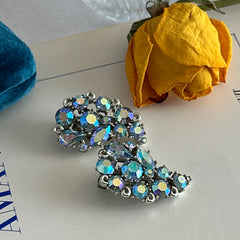 Vintage Lisner silver tone clip-on earrings with blue Aurora Borealis rhinestones in a leaf-shaped climber design, shown in various arrangements.