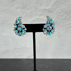 Vintage Lisner silver tone clip-on earrings with blue Aurora Borealis rhinestones in a leaf-shaped climber design, shown in various arrangements.