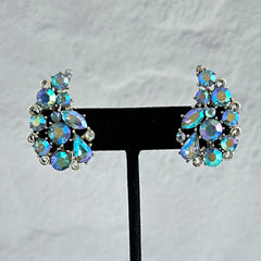 Vintage Lisner silver tone clip-on earrings with blue Aurora Borealis rhinestones in a leaf-shaped climber design, shown in various arrangements.