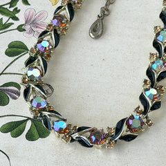 Vintage Lisner aurora‑borealis topaz and black enamel gold‑tone floral necklace with adjustable hook clasp and hangtag, shown on botanical background to highlight sparkle and craftsmanship.