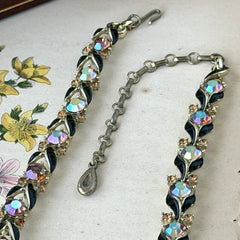Vintage Lisner aurora‑borealis topaz and black enamel gold‑tone floral necklace with adjustable hook clasp and hangtag, shown on botanical background to highlight sparkle and craftsmanship.