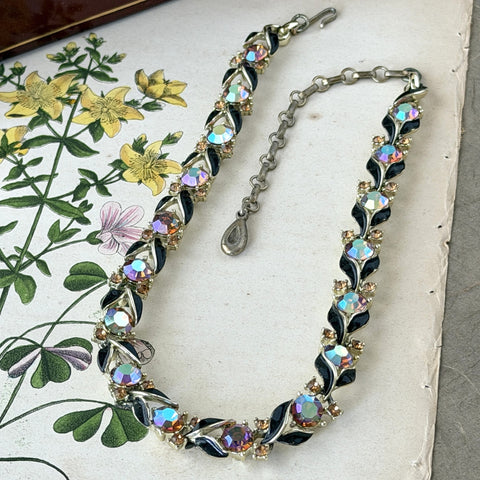 Vintage Lisner aurora‑borealis topaz and black enamel gold‑tone floral necklace with adjustable hook clasp and hangtag, shown on botanical background to highlight sparkle and craftsmanship.