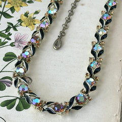 Vintage Lisner aurora‑borealis topaz and black enamel gold‑tone floral necklace with adjustable hook clasp and hangtag, shown on botanical background to highlight sparkle and craftsmanship.