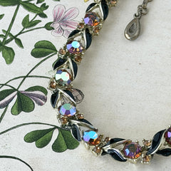 Vintage Lisner aurora‑borealis topaz and black enamel gold‑tone floral necklace with adjustable hook clasp and hangtag, shown on botanical background to highlight sparkle and craftsmanship.