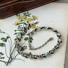 Vintage Lisner aurora‑borealis topaz and black enamel gold‑tone floral necklace with adjustable hook clasp and hangtag, shown on botanical background to highlight sparkle and craftsmanship.