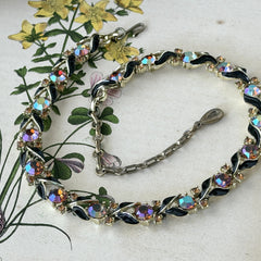 Vintage Lisner aurora‑borealis topaz and black enamel gold‑tone floral necklace with adjustable hook clasp and hangtag, shown on botanical background to highlight sparkle and craftsmanship.