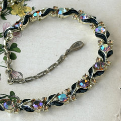 Vintage Lisner aurora‑borealis topaz and black enamel gold‑tone floral necklace with adjustable hook clasp and hangtag, shown on botanical background to highlight sparkle and craftsmanship.