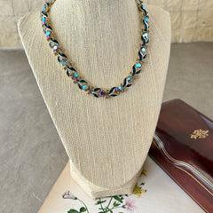 Vintage Lisner aurora‑borealis topaz and black enamel gold‑tone floral necklace with adjustable hook clasp and hangtag, shown on botanical background to highlight sparkle and craftsmanship.