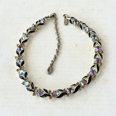 Vintage Lisner aurora‑borealis topaz and black enamel gold‑tone floral necklace with adjustable hook clasp and hangtag, shown on botanical background to highlight sparkle and craftsmanship.