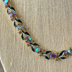 Vintage Lisner aurora‑borealis topaz and black enamel gold‑tone floral necklace with adjustable hook clasp and hangtag, shown on botanical background to highlight sparkle and craftsmanship.