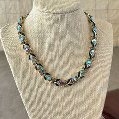 Vintage Lisner aurora‑borealis topaz and black enamel gold‑tone floral necklace with adjustable hook clasp and hangtag, shown on botanical background to highlight sparkle and craftsmanship.