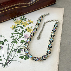 Vintage Lisner aurora‑borealis topaz and black enamel gold‑tone floral necklace with adjustable hook clasp and hangtag, shown on botanical background to highlight sparkle and craftsmanship.