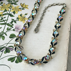 Vintage Lisner aurora‑borealis topaz and black enamel gold‑tone floral necklace with adjustable hook clasp and hangtag, shown on botanical background to highlight sparkle and craftsmanship.