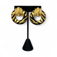 Vintage Elizabeth Taylor for Avon Zebra Stripes clip-on earrings from 1994, featuring bold black enamel and gold-tone door knocker design with sculpted horse and ram head motifs, accented by rhinestones. Signed “Elizabeth Taylor Avon” on the back.