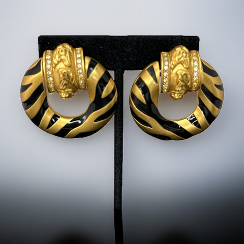 Vintage Elizabeth Taylor for Avon Zebra Stripes clip-on earrings from 1994, featuring bold black enamel and gold-tone door knocker design with sculpted horse and ram head motifs, accented by rhinestones. Signed “Elizabeth Taylor Avon” on the back.