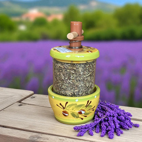 Hand-painted Provence herb mill with green, yellow, and brown olive branch motif on ceramic base, featuring a transparent chamber filled with dried herbs and topped with a wooden handle and cork stoppers.