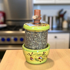 Hand-painted Provence herb mill with green, yellow, and brown olive branch motif on ceramic base, featuring a transparent chamber filled with dried herbs and topped with a wooden handle and cork stoppers.