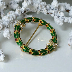 Vintage MMA Fabergé replica Christmas wreath brooch with green guilloché enamel leaves, red berry accents, clear rhinestone ribbon details, and gold‑plated finish; signed MMA © FBS, excellent condition