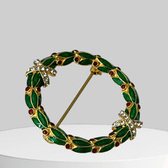 Vintage MMA Fabergé replica Christmas wreath brooch with green guilloché enamel leaves, red berry accents, clear rhinestone ribbon details, and gold‑plated finish; signed MMA © FBS, excellent condition