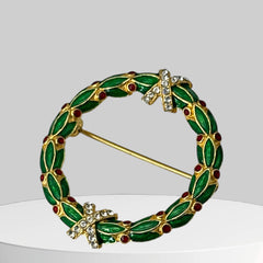Vintage MMA Fabergé replica Christmas wreath brooch with green guilloché enamel leaves, red berry accents, clear rhinestone ribbon details, and gold‑plated finish; signed MMA © FBS, excellent condition