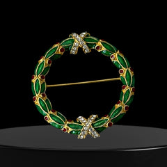 Vintage MMA Fabergé replica Christmas wreath brooch with green guilloché enamel leaves, red berry accents, clear rhinestone ribbon details, and gold‑plated finish; signed MMA © FBS, excellent condition