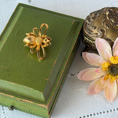 Vintage Mamselle gold‑tone bumblebee brooch with textured body and looped wings, signed on back, shown with floral and box props.