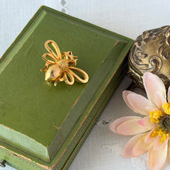 Vintage Mamselle gold‑tone bumblebee brooch with textured body and looped wings, signed on back, shown with floral and box props.