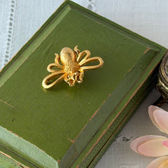 Vintage Mamselle gold‑tone bumblebee brooch with textured body and looped wings, signed on back, shown with floral and box props.