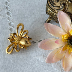 Vintage Mamselle gold‑tone bumblebee brooch with textured body and looped wings, signed on back, shown with floral and box props.