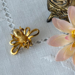 Vintage Mamselle gold‑tone bumblebee brooch with textured body and looped wings, signed on back, shown with floral and box props.