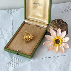 Vintage Mamselle gold‑tone bumblebee brooch with textured body and looped wings, signed on back, shown with floral and box props.
