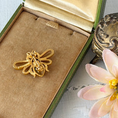 Vintage Mamselle gold‑tone bumblebee brooch with textured body and looped wings, signed on back, shown with floral and box props.