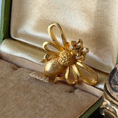 Vintage Mamselle gold‑tone bumblebee brooch with textured body and looped wings, signed on back, shown with floral and box props.