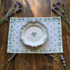 Reversible quilted cotton placemat in Lauris Light Green by Marat d’Avignon, featuring a white center with lavender purple floral medallions and a border of lavender sprigs and olive branches, with a white reverse side  scattered with tiny lavender  blossoms, crafted in Provence.