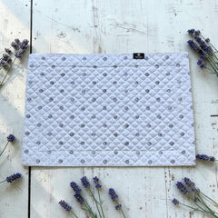Reversible quilted cotton placemat in Lauris Light Green by Marat d’Avignon, featuring a white center with lavender purple floral medallions and a border of lavender sprigs and olive branches, with a white reverse side  scattered with tiny lavender  blossoms, crafted in Provence.