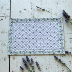 Reversible quilted cotton placemat in Lauris Light Green by Marat d’Avignon, featuring a white center with lavender purple floral medallions and a border of lavender sprigs and olive branches, with a white reverse side  scattered with tiny lavender  blossoms, crafted in Provence.