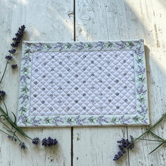 Reversible quilted cotton placemat in Lauris Light Green by Marat d’Avignon, featuring a white center with lavender purple floral medallions and a border of lavender sprigs and olive branches, with a white reverse side  scattered with tiny lavender  blossoms, crafted in Provence.