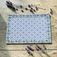Reversible quilted cotton placemat in Lauris Light Green by Marat d’Avignon, featuring a white center with lavender purple floral medallions and a border of lavender sprigs and olive branches, with a white reverse side  scattered with tiny lavender  blossoms, crafted in Provence.