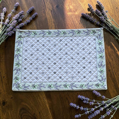 Reversible quilted cotton placemat in Lauris Light Green by Marat d’Avignon, featuring a white center with lavender purple floral medallions and a border of lavender sprigs and olive branches, with a white reverse side  scattered with tiny lavender  blossoms, crafted in Provence.