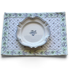 Reversible quilted cotton placemat in Lauris Light Green by Marat d’Avignon, featuring a white center with lavender purple floral medallions and a border of lavender sprigs and olive branches, with a white reverse side  scattered with tiny lavender  blossoms, crafted in Provence.