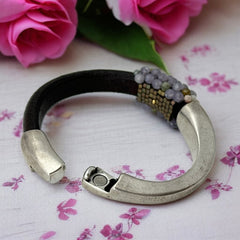 Brown leather and silver-tone half cuff bracelet with magnetic clasp, hand-stitched faceted purple and green amethyst beads, featuring a signature gold accent bead; size 6.