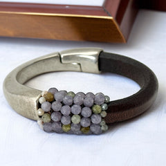 Brown leather and silver-tone half cuff bracelet with magnetic clasp, hand-stitched faceted purple and green amethyst beads, featuring a signature gold accent bead; size 6.