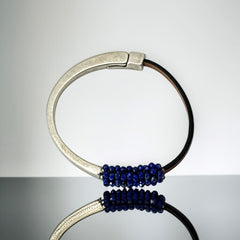 Artisan bracelet featuring a silver-tone half cuff and brown leather band, hand-stitched with faceted lapis beads and a signature gold accent; Martell Studio design, size 6 with magnetic clasp.